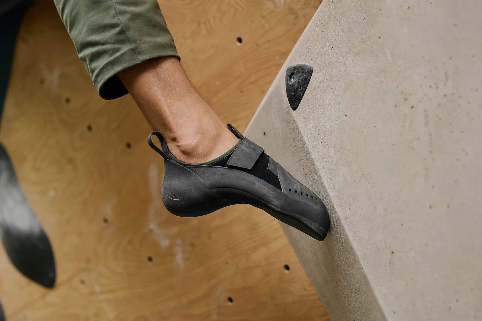 Close view of a black downturned climbing shoe pressing its toe into the face of a pale sloping indoor volume.